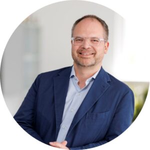 Headshot of Gerald Reichmann, CFO of adapa Group, wearing glasses and a business suit, smiling confidently.