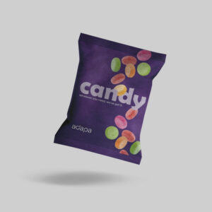 web-optimised-paperflow_candy A dark purple paper-based pillow pouch packaging floating at an angle against a solid light gray background. The front of the pouch features the word "candy" in a large, stylized white font, with the tagline "Whatever you need, we've got it!" printed underneath. Colorful hard candies in shades of green, red, orange, and pink are illustrated cascading down the packaging, and the white "adapa" brand logo is positioned in the bottom-left corner.